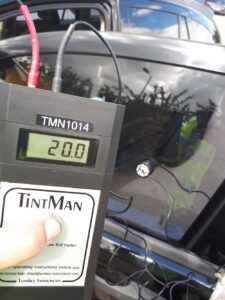 A handheld meter checks a car window's tint level