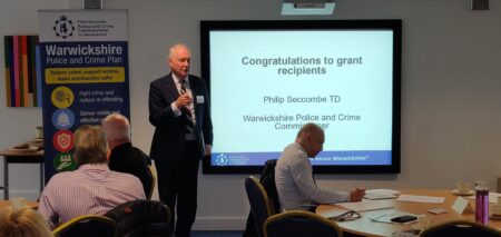 Philip Seccombe addresses the room in front of a welcome sign to attendees