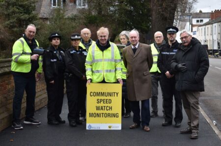 A group of people stand behind a Community Speed Watch sign