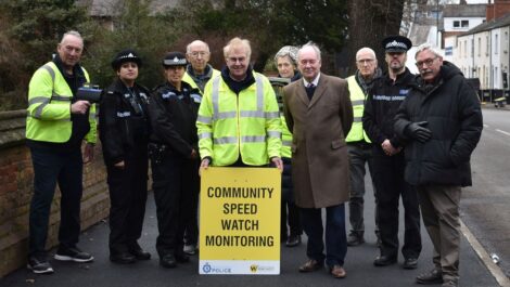 A group of people stand behind a Community Speed Watch sign