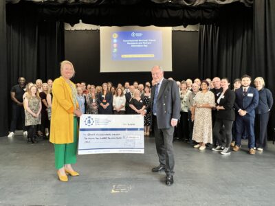 The Deputy PCC and PCC stand with a giant cheque for £2.2m in front of a group of people