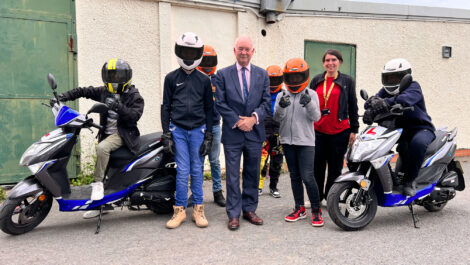 The Commissioner stands with a group of young moped riders in helmets.